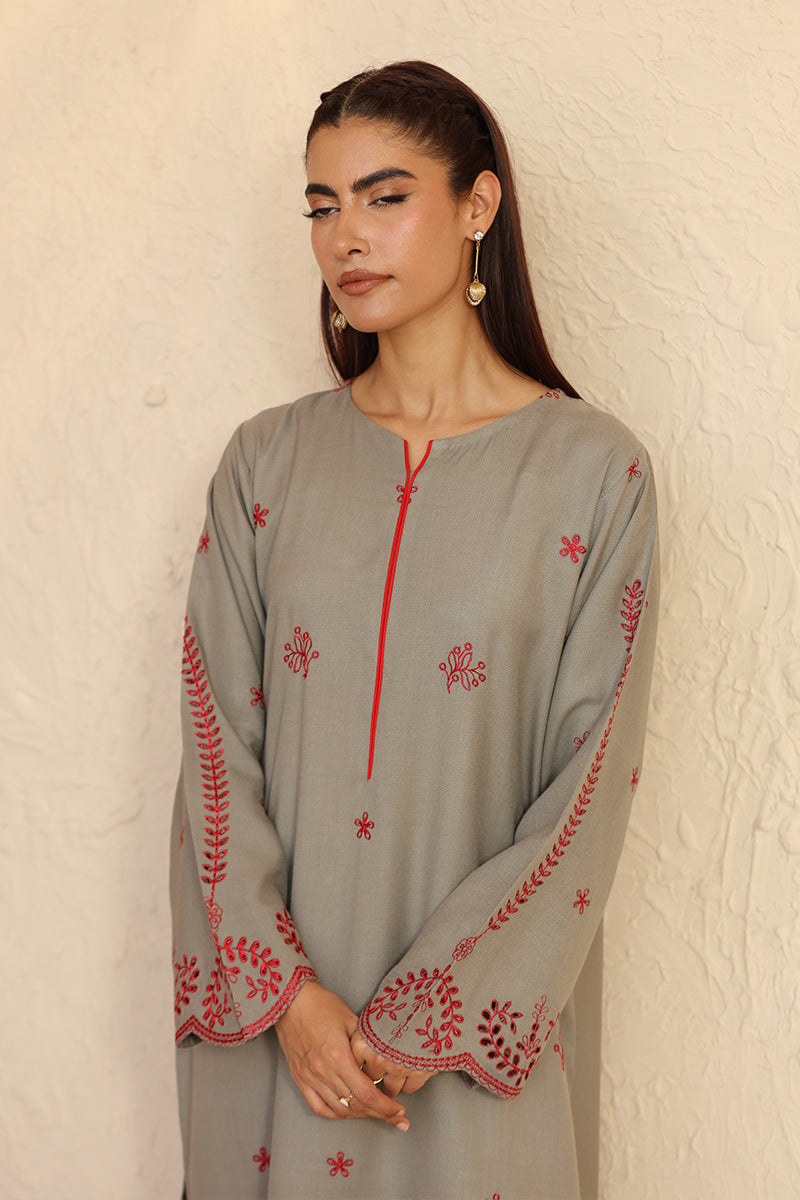 Woman wearing a gray embroidered dress against a beige wall