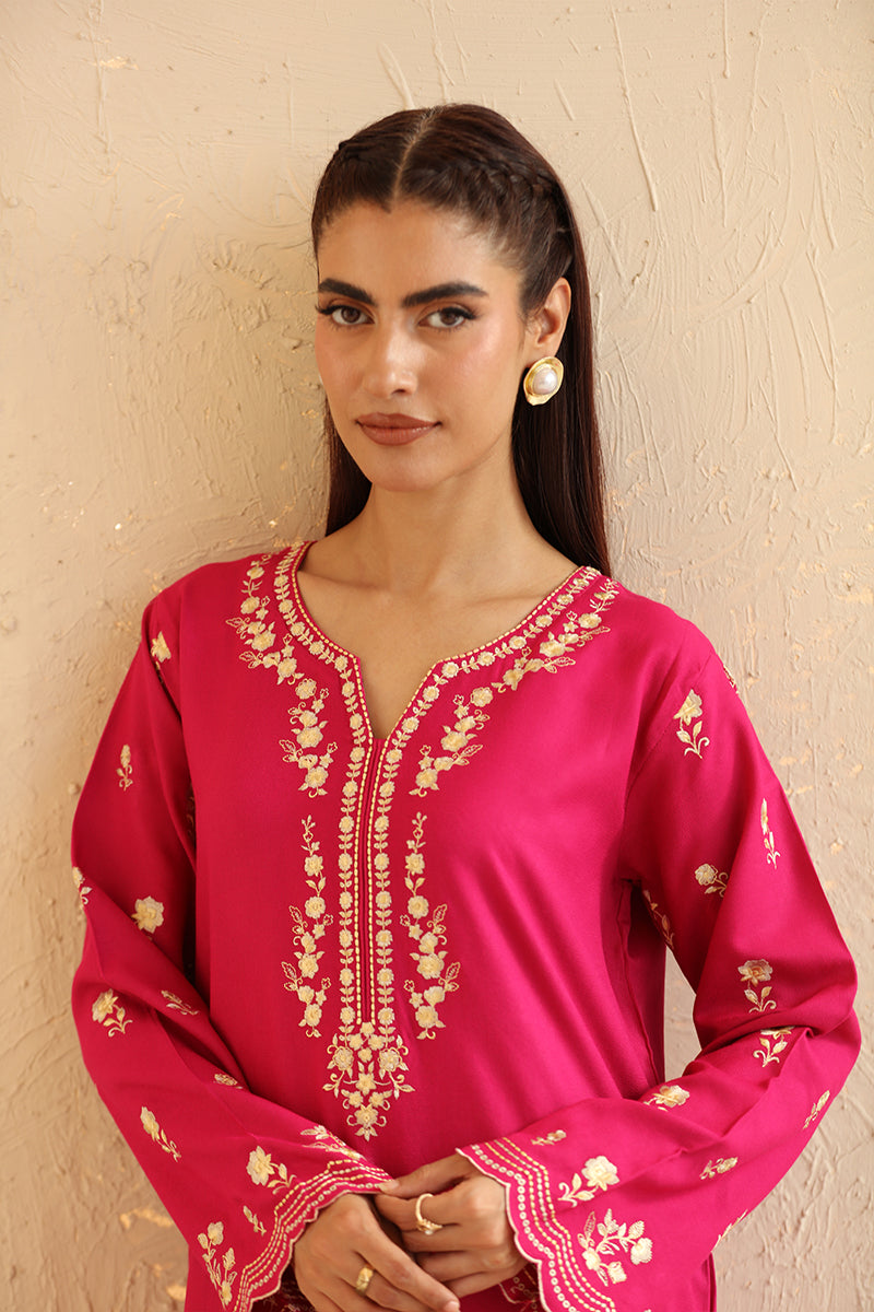 Woman wearing a pink embroidered top against a beige wall