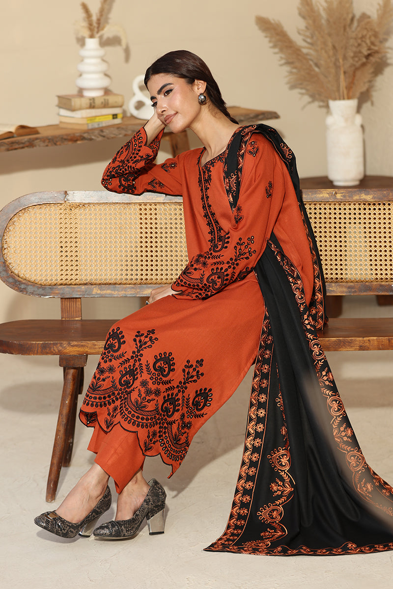 Woman in an orange and black embroidered outfit sitting on a wooden chair.