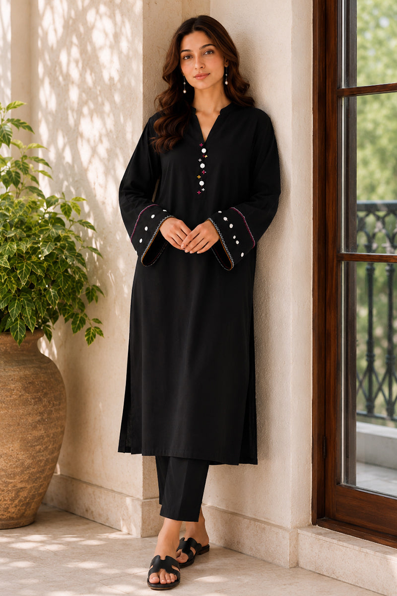 Woman in a black outfit standing by a window with a plant nearby