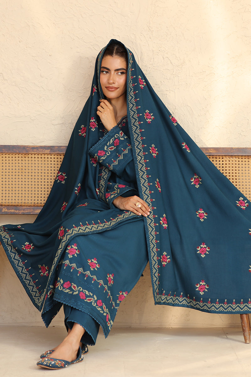 Woman wearing a blue embroidered traditional outfit sitting on a wooden bench.