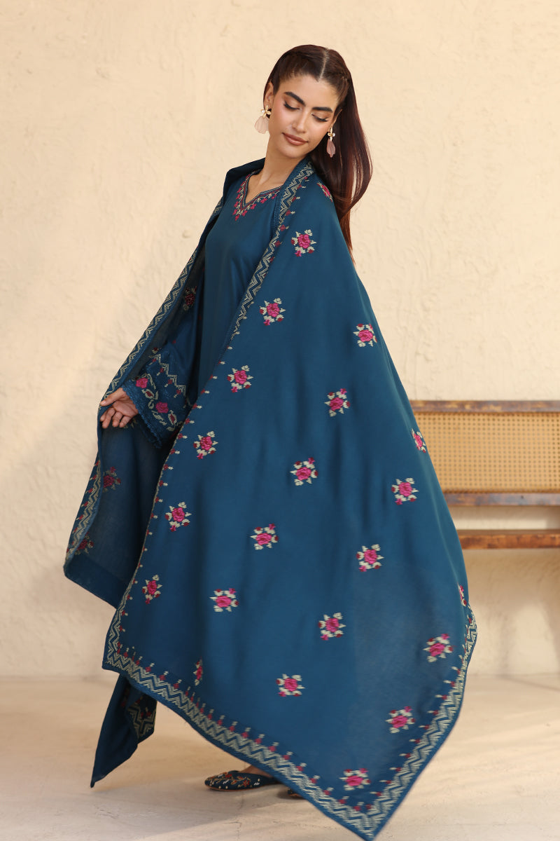 Woman wearing a blue embroidered traditional outfit against a beige background