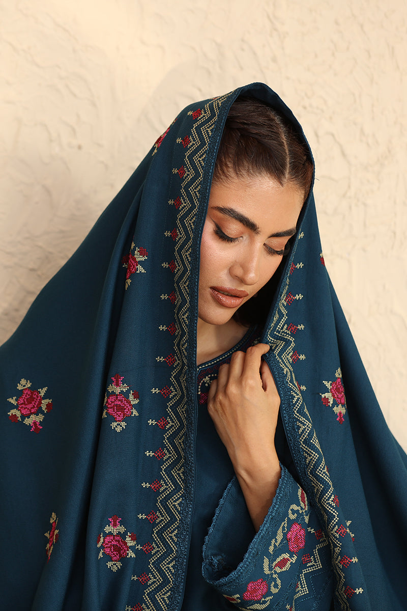 Woman wearing a dark blue embroidered hijab against a beige wall