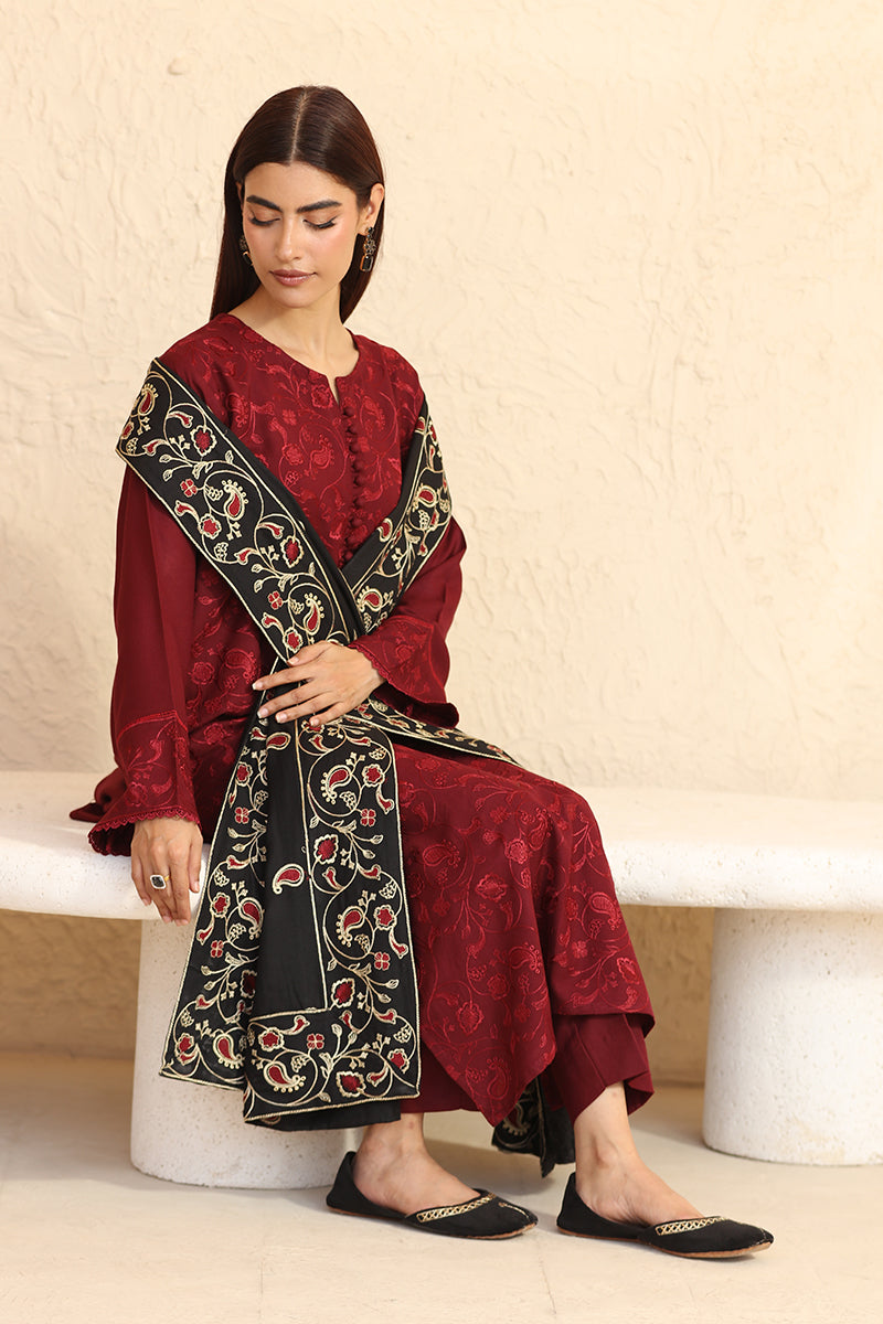 Woman wearing a maroon traditional outfit with black embroidery sitting on a white bench.
