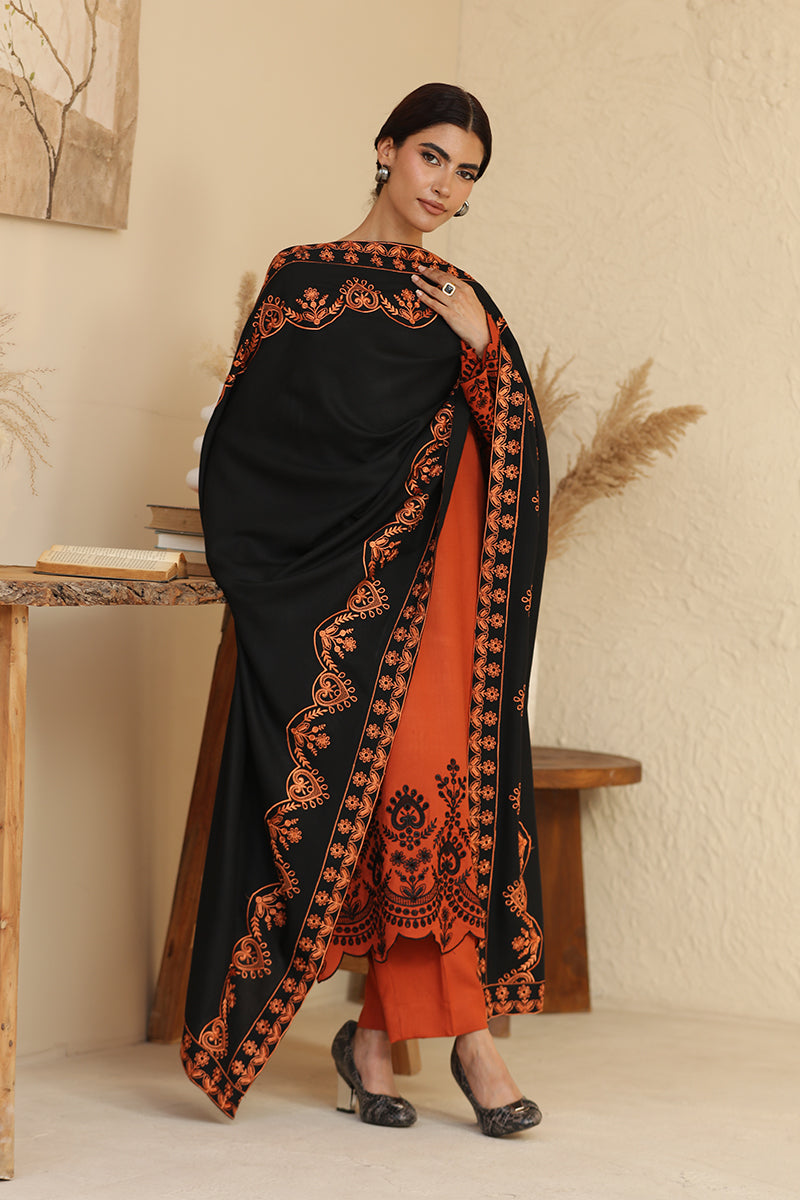 Woman wearing a black and orange embroidered saree in a minimalistic setting.