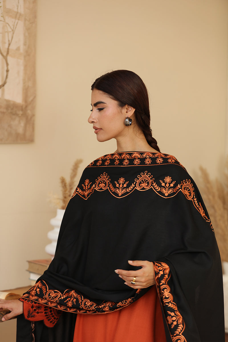 Woman wearing a black and orange embroidered traditional outfit indoors.