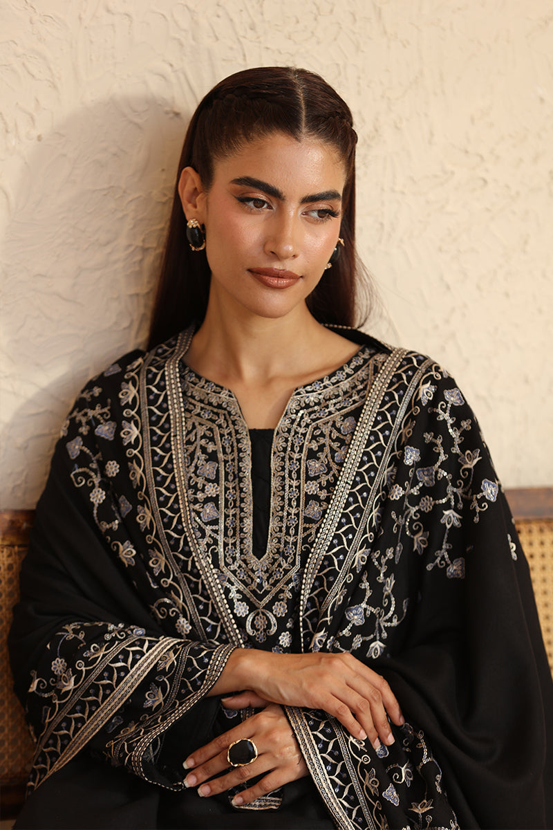 Woman wearing a black embroidered abaya against a textured wall.