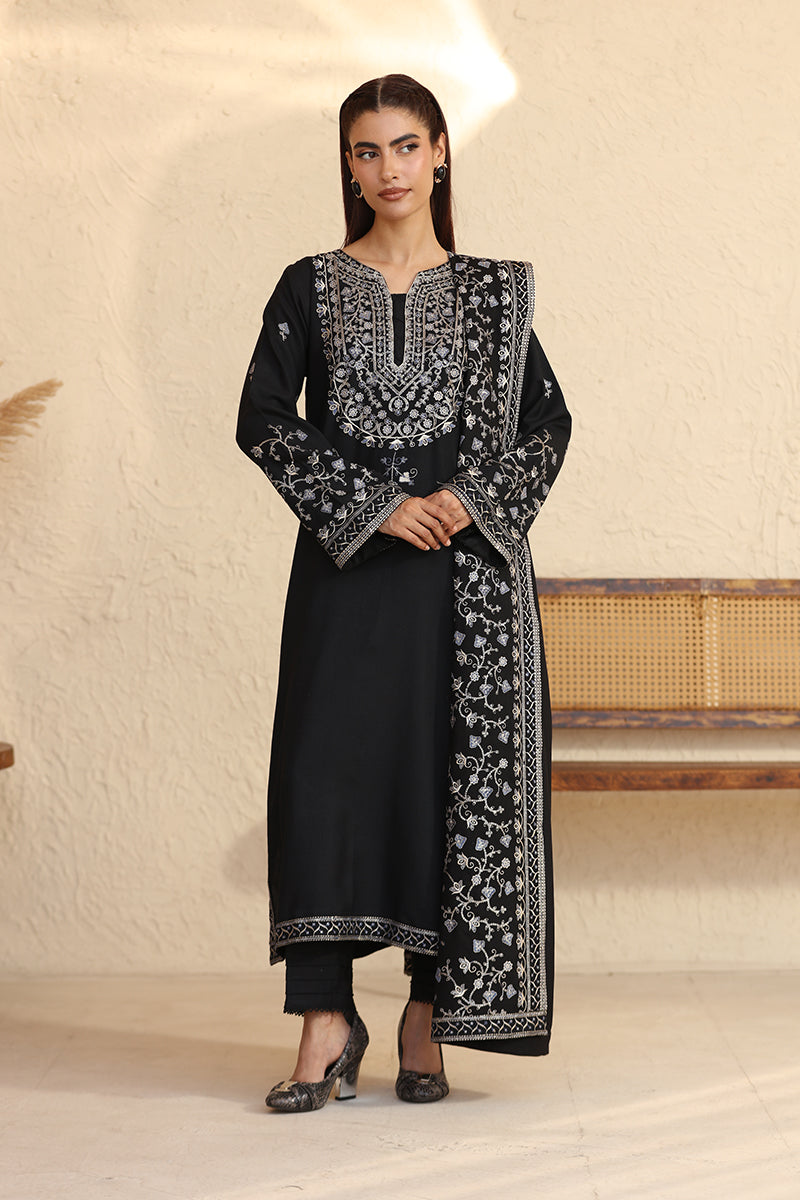 Woman wearing a black embroidered traditional outfit in a minimalistic setting
