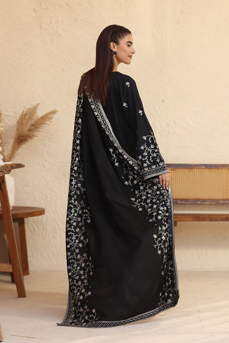 Woman wearing a black abaya with floral patterns in a minimal indoor setting