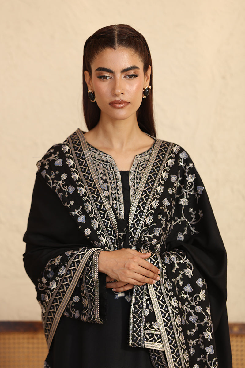 Woman wearing a black embroidered abaya against a beige background