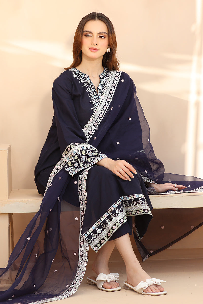 Woman wearing a navy blue embroidered outfit with a sheer dupatta, sitting on a bench.