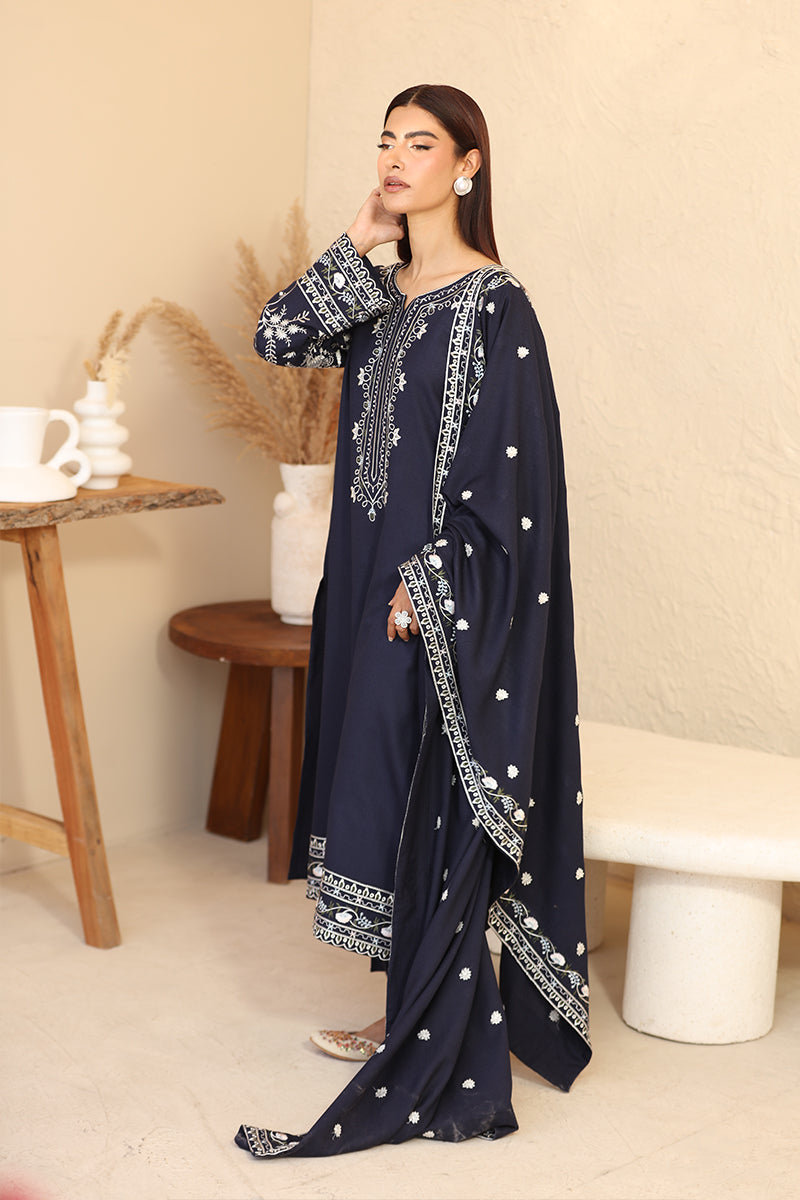 Woman wearing a navy blue traditional outfit with white patterns in a minimalistic setting.