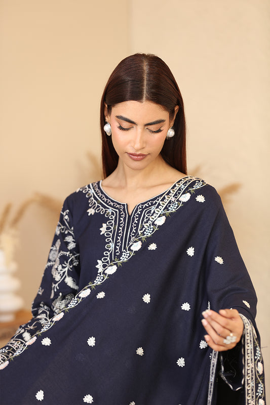 Woman wearing a navy blue embroidered traditional outfit with white patterns on a beige background