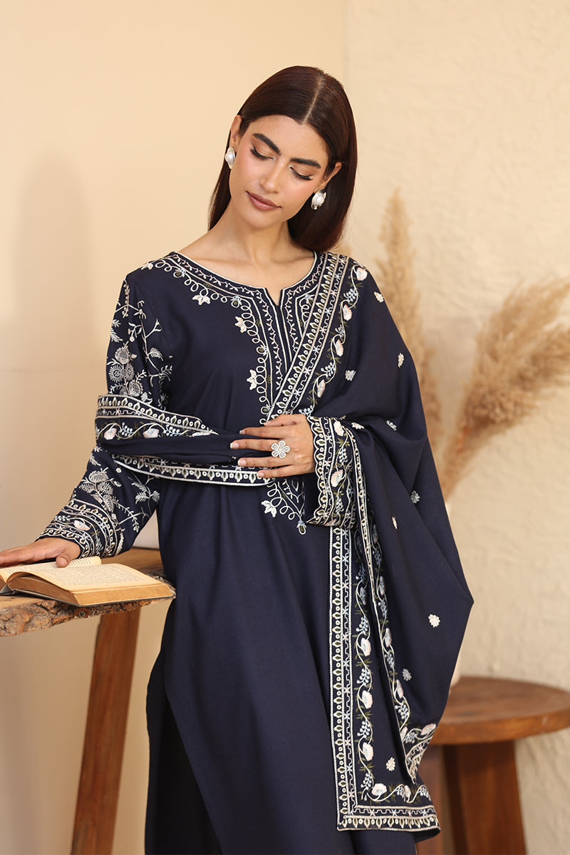 Woman wearing a navy blue embroidered dress sitting on a wooden stool.