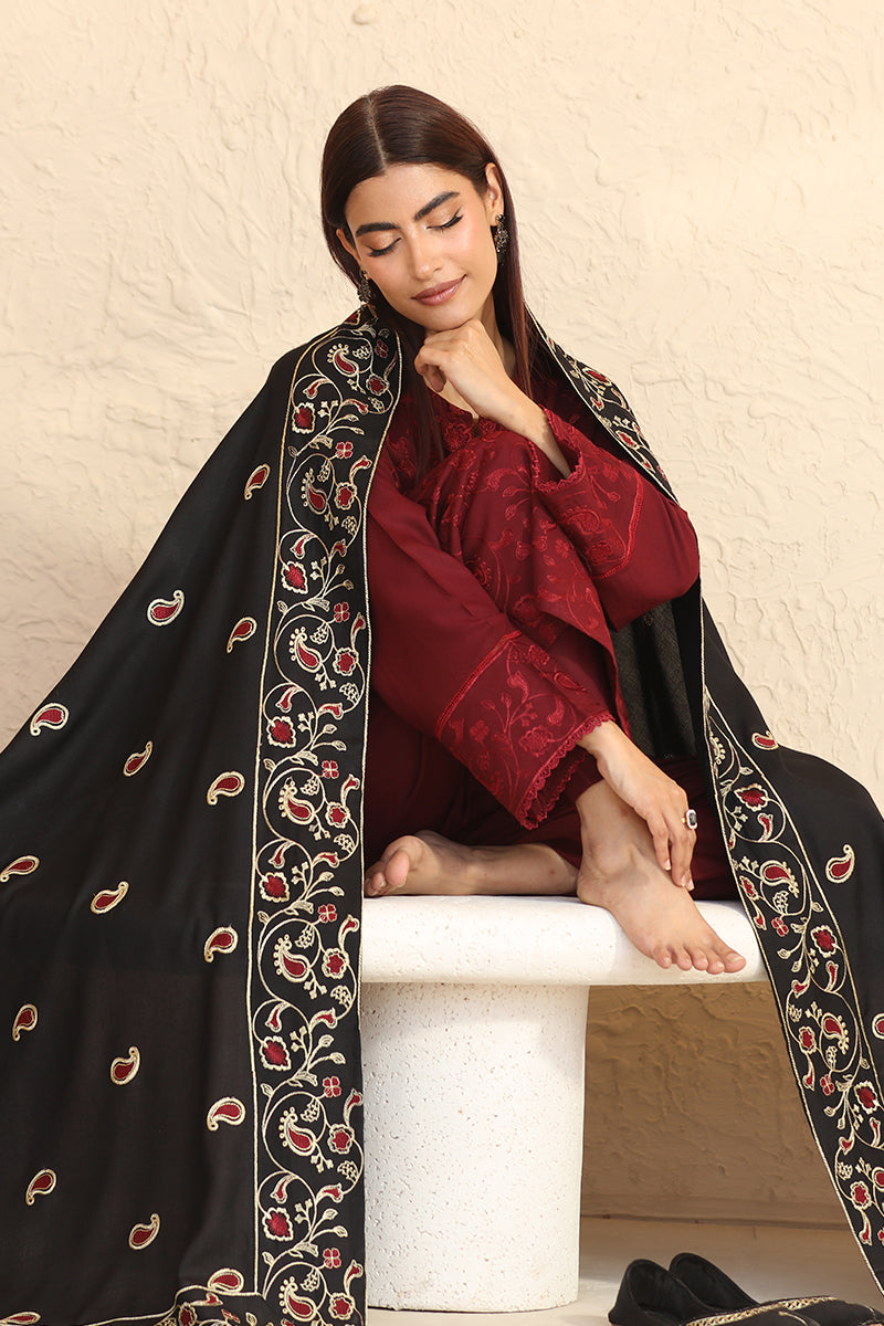 Woman wearing a black embroidered scarf and red top sitting on a white stool.