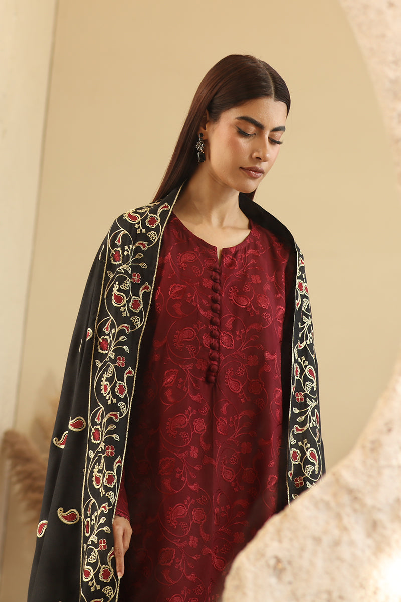 Woman wearing a red kurta with a black embroidered shawl against a beige background