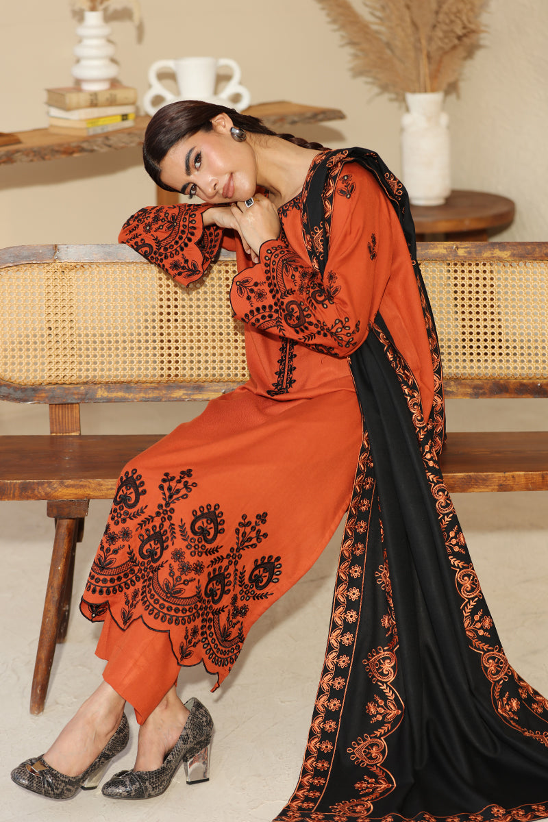 Woman wearing an orange and black embroidered outfit sitting on a wooden bench.