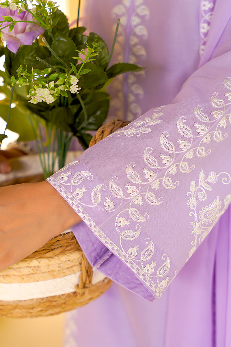 Purple fabric with white embroidery held by a hand, with flowers and a woven basket in the background.