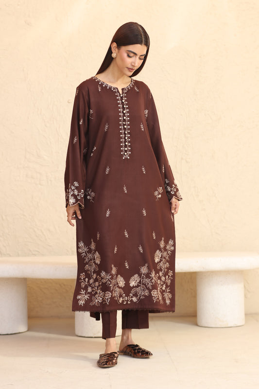 Woman wearing a brown embroidered kurta with white patterns against a beige background