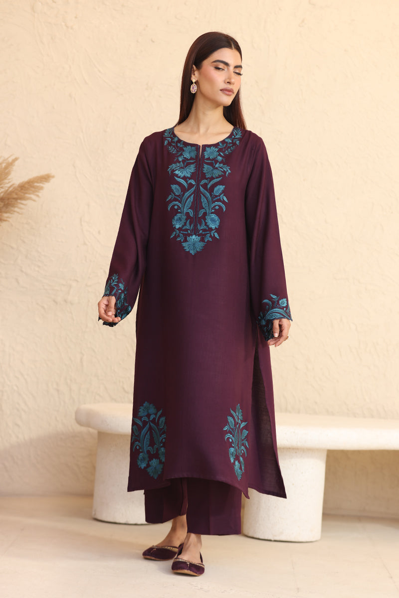 Woman wearing a dark purple embroidered dress with a beige background