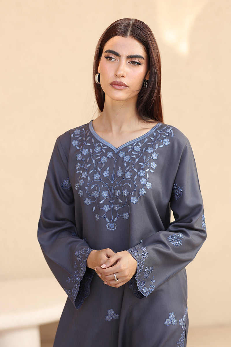 Woman wearing a dark gray dress with floral embroidery on a beige background