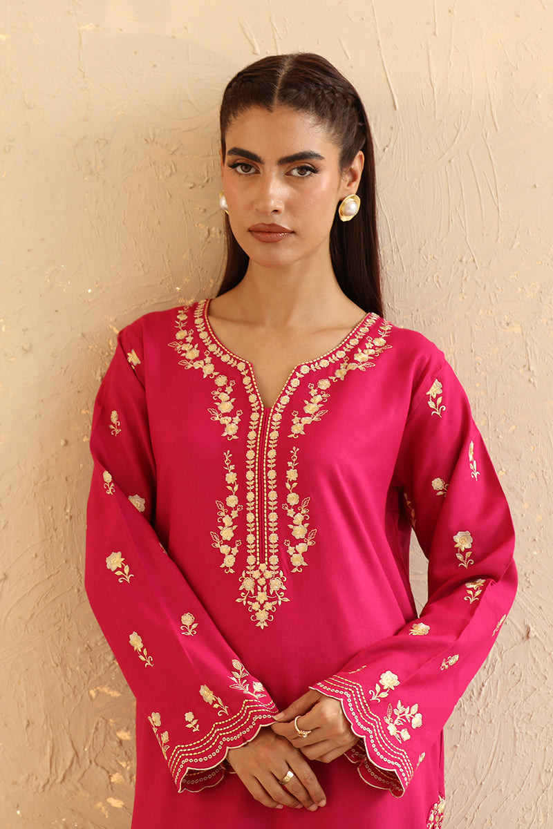 Woman wearing a pink embroidered traditional outfit against a beige wall