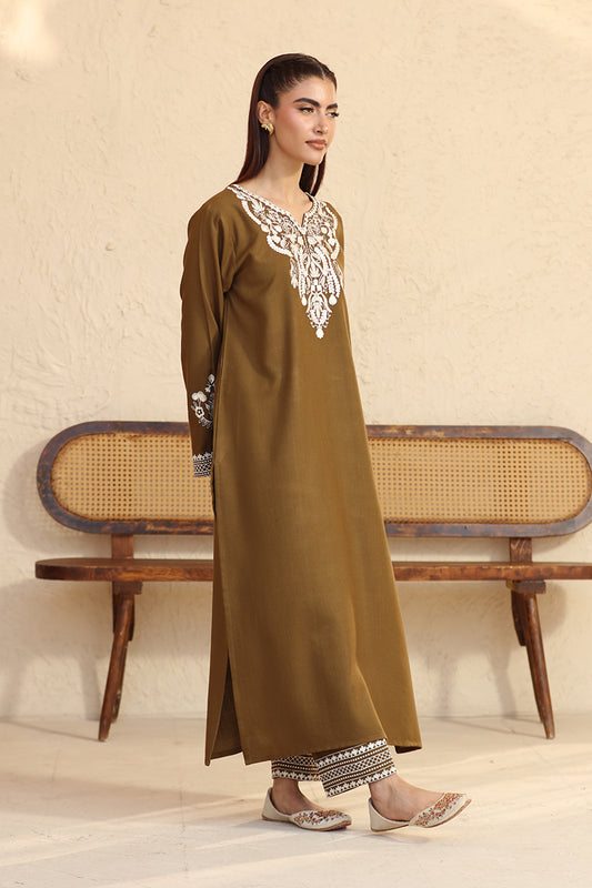 Woman wearing a brown dress with white embroidery in a minimalistic setting