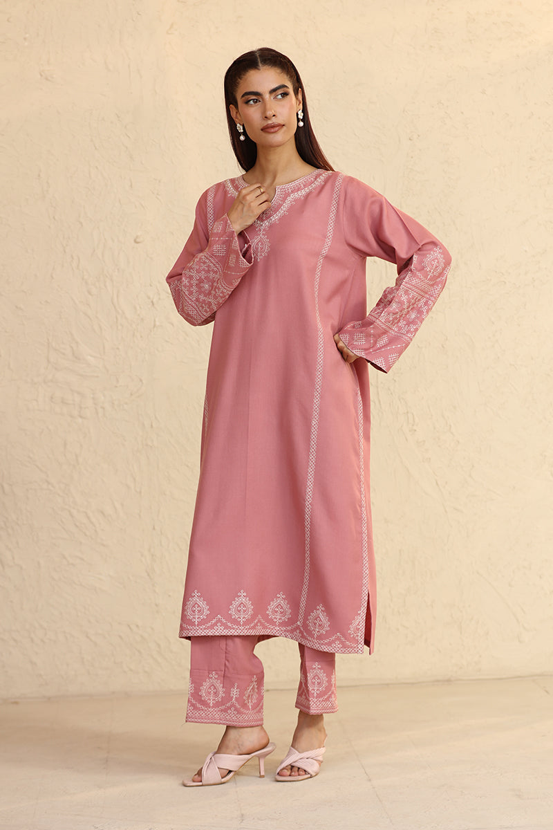 Woman wearing a pink traditional outfit with white embroidery against a beige background