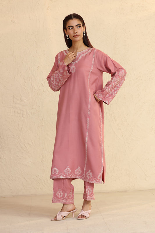 Woman wearing a pink traditional outfit with white embroidery against a beige background