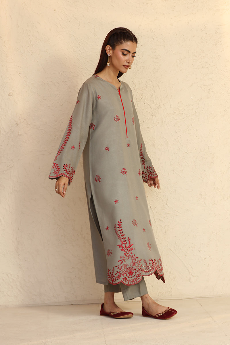 Woman wearing a light gray kurta with red floral embroidery against a beige background