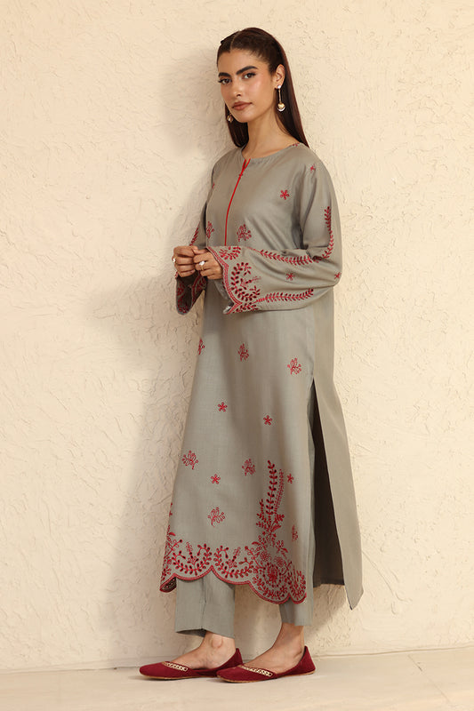 Woman wearing a gray kurta with red embroidery against a beige background