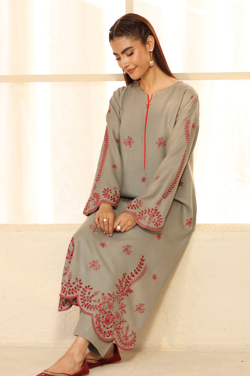 Woman wearing a gray dress with red embroidery sitting on a white couch.