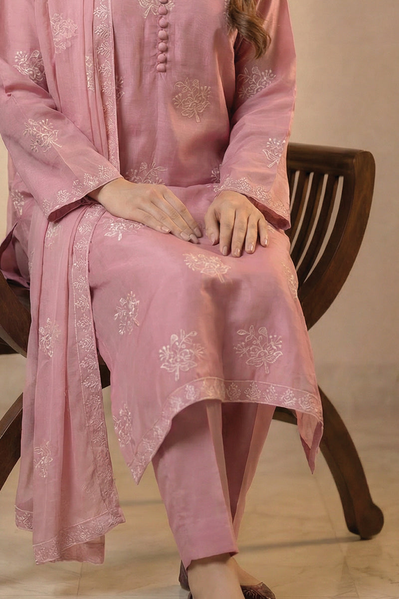 Person wearing a pink embroidered traditional outfit sitting on a wooden chair.