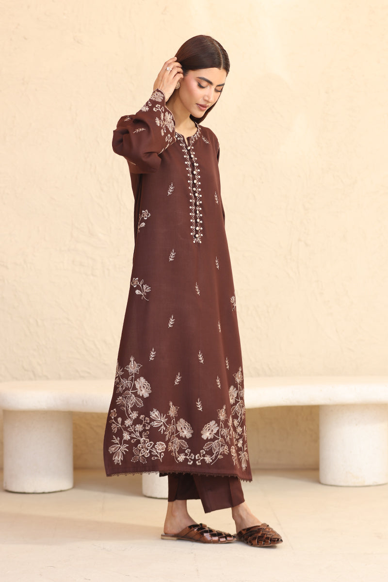 Woman wearing a brown embroidered outfit against a beige background