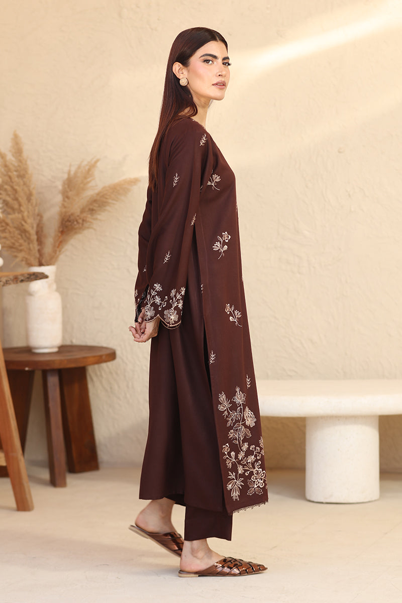 Woman wearing a brown embroidered outfit in a minimalistic room.