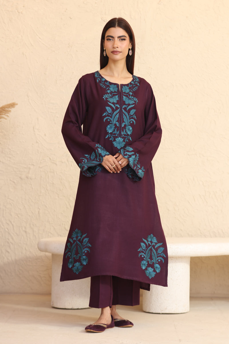 Woman wearing a dark purple outfit with blue embroidery against a beige background