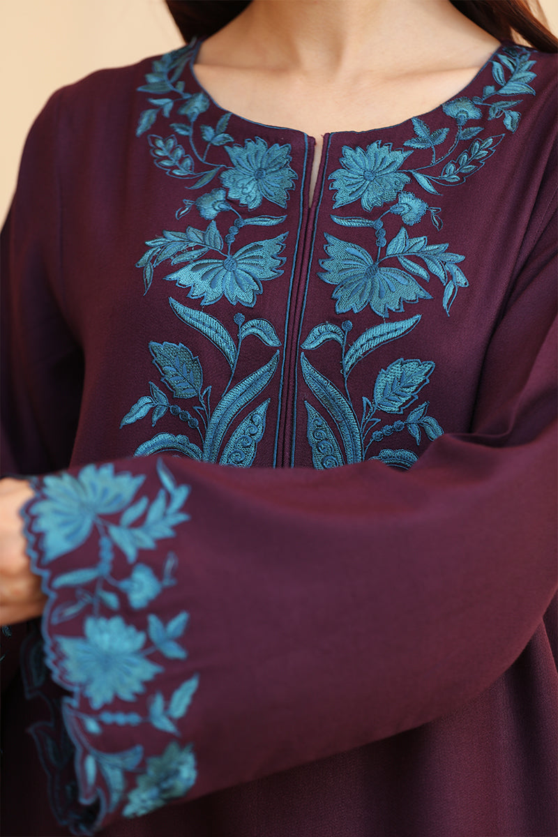Close-up of a maroon garment with blue floral embroidery