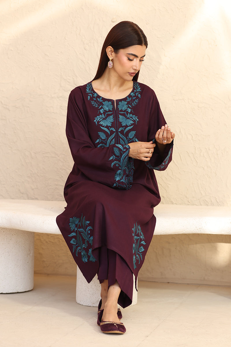 Woman wearing a dark purple outfit with teal embroidery sitting on a white bench.