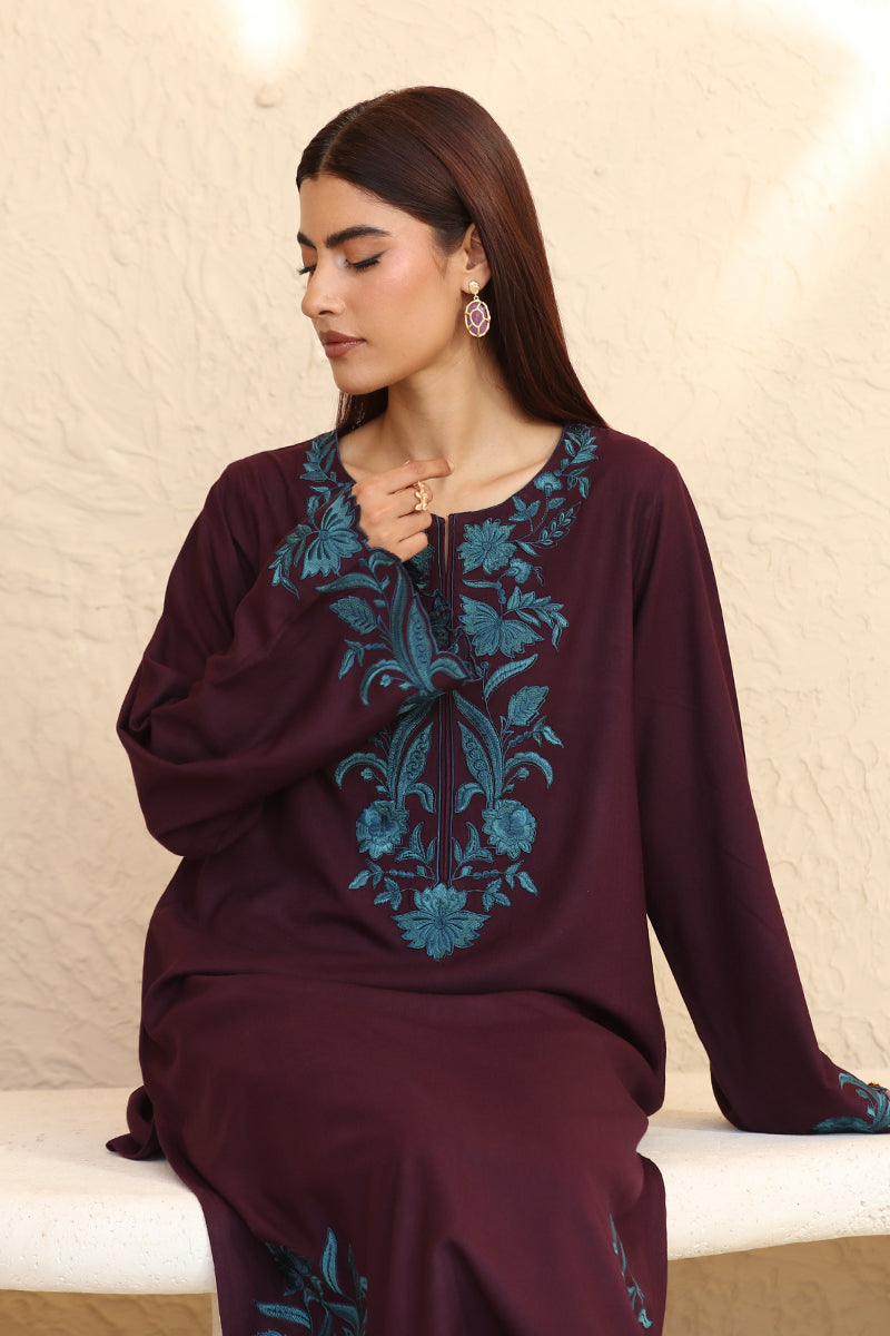 Woman wearing a maroon outfit with blue floral embroidery sitting on a white surface.