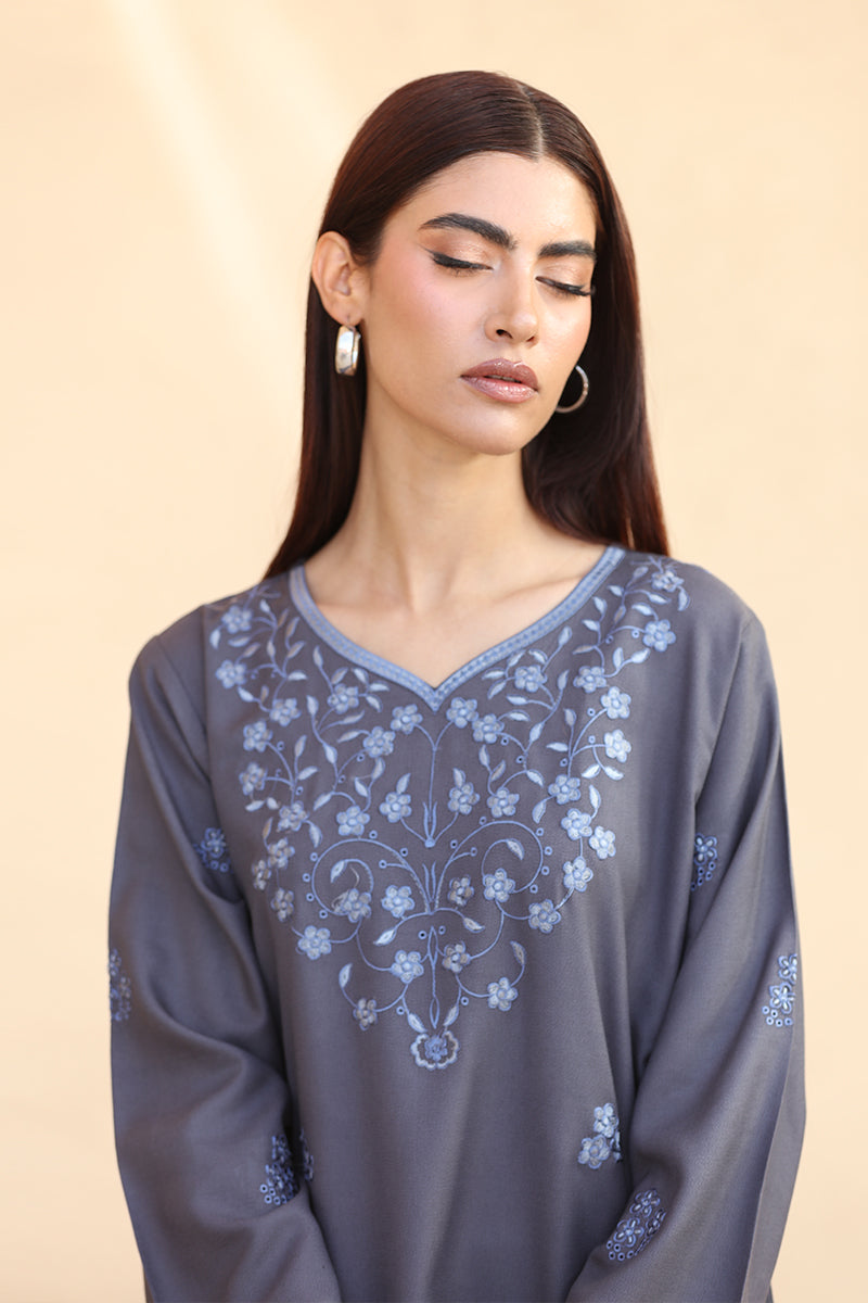 Woman wearing a gray dress with floral embroidery on a beige background