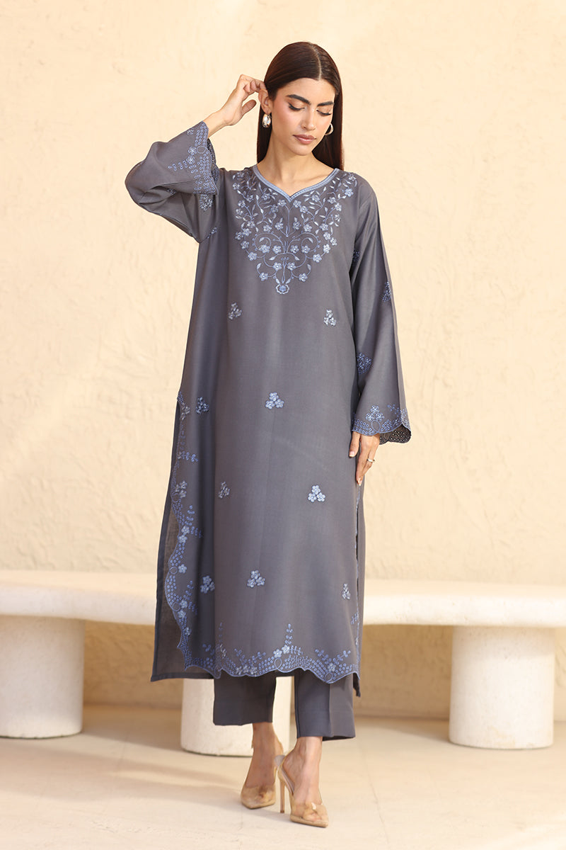 Woman wearing a gray embroidered dress against a beige background