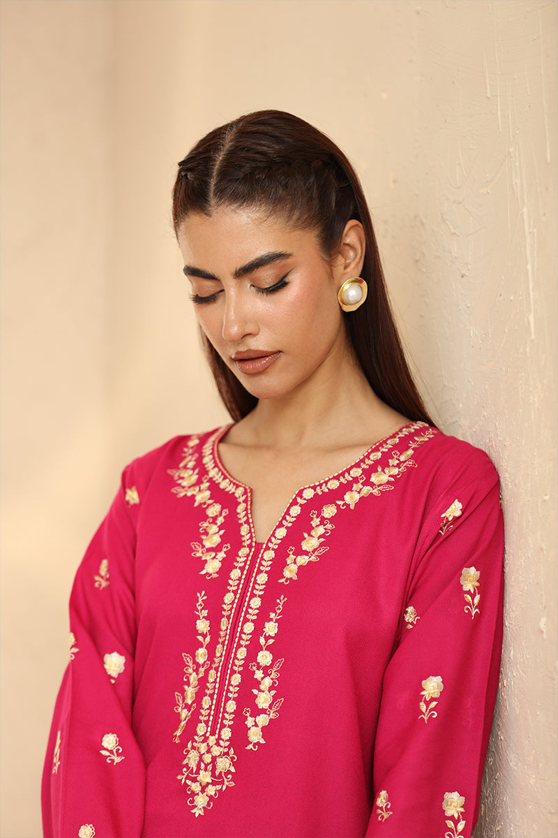 Woman wearing a pink embroidered top against a beige wall