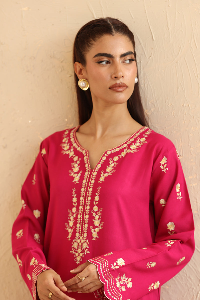 Woman wearing a pink embroidered traditional outfit against a beige background