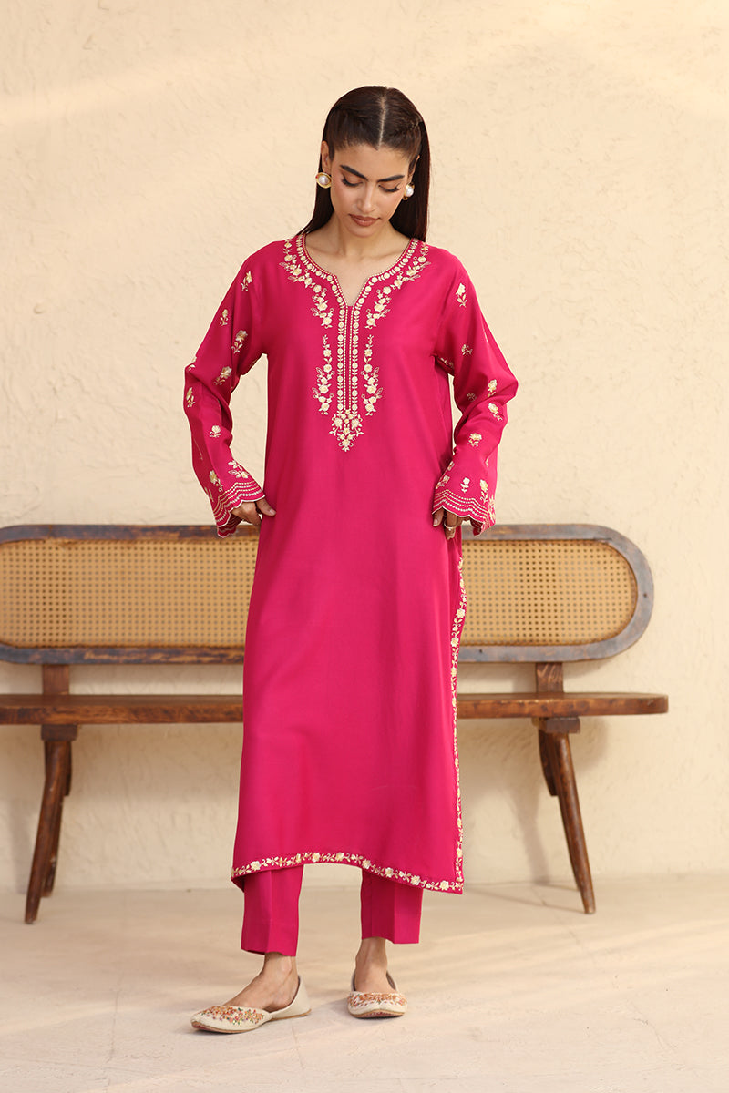 Woman wearing a pink embroidered traditional outfit with a beige background
