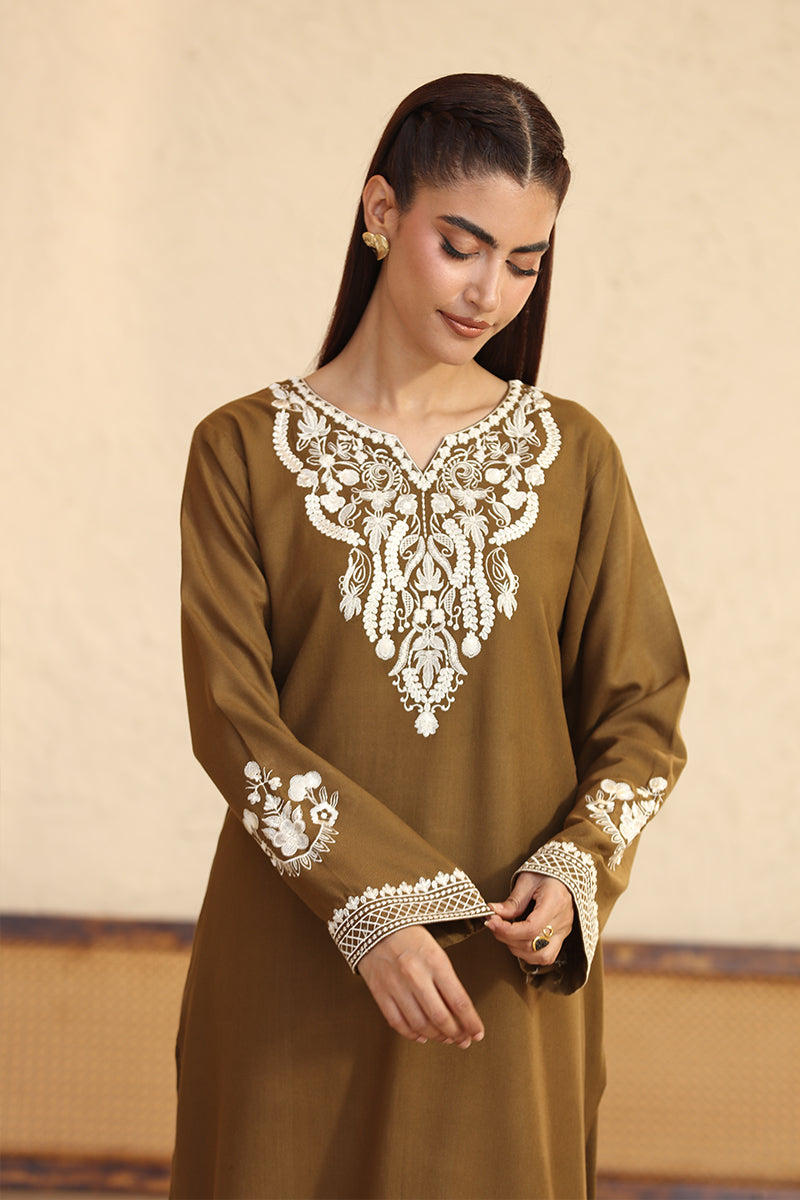 Woman wearing a brown dress with white embroidery against a beige background