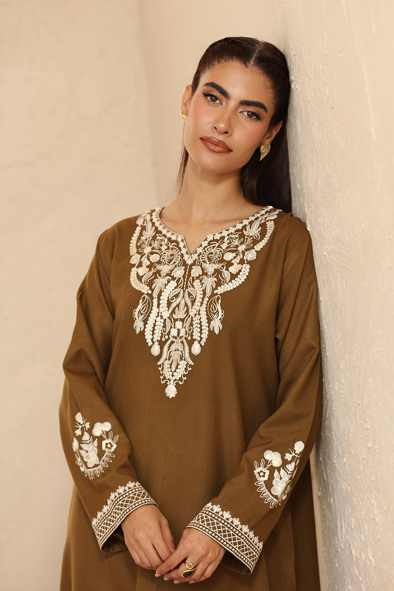 Woman wearing a brown embroidered dress against a beige wall