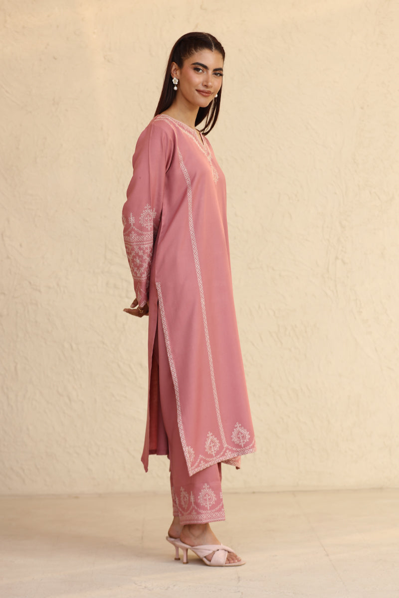 Woman wearing a pink traditional outfit with embroidery against a beige background