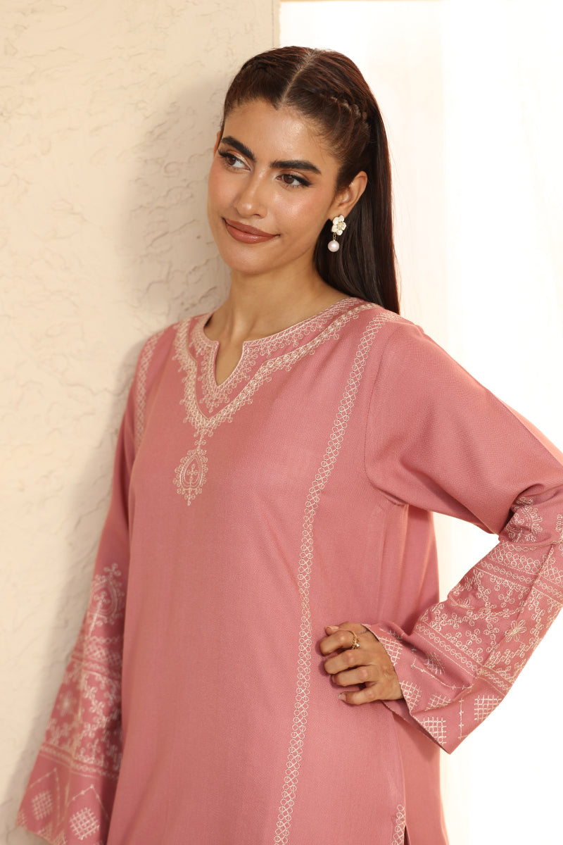 Woman wearing a pink embroidered traditional outfit against a light background