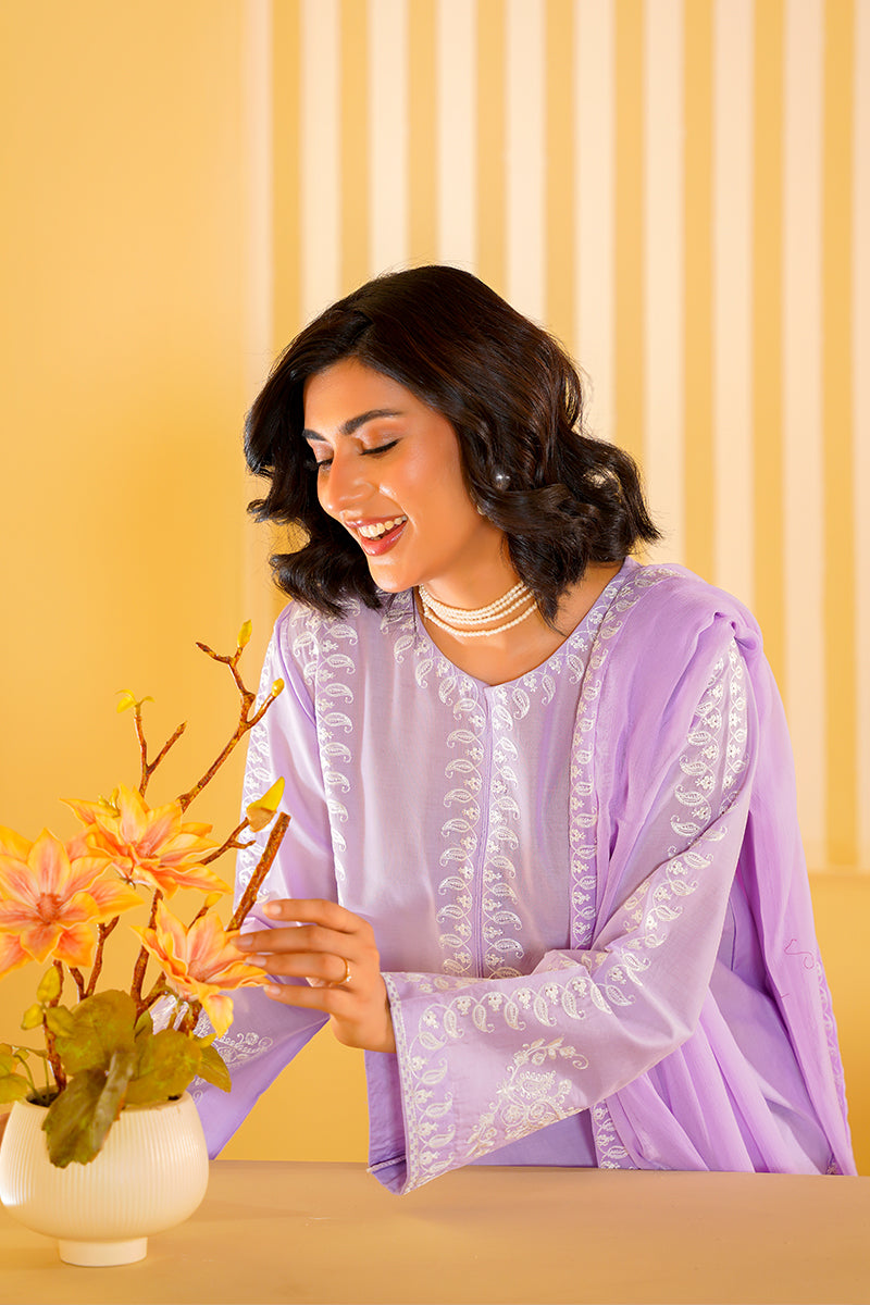 Woman in a light purple traditional outfit with floral decorations on a yellow background