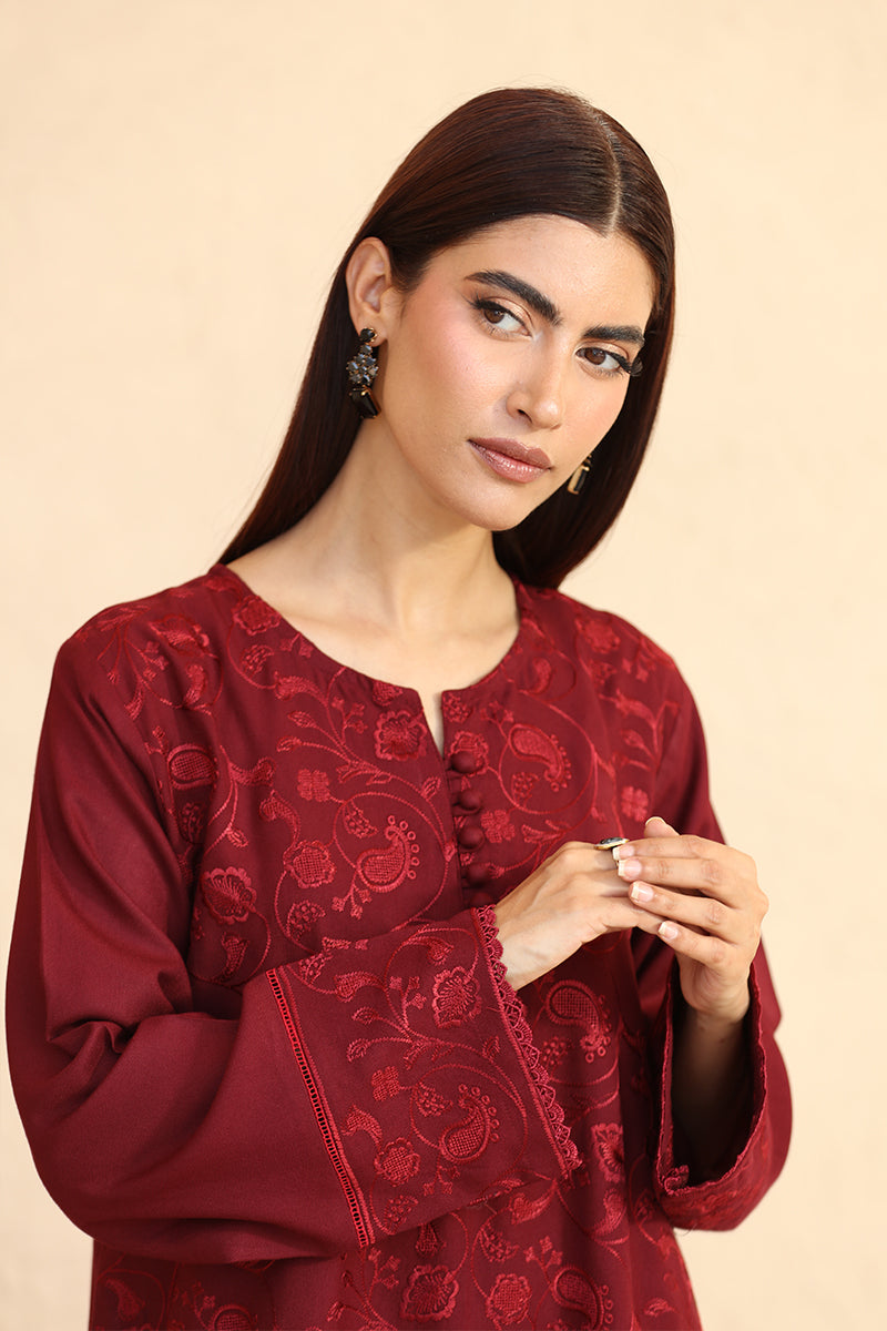 Woman wearing a red embroidered traditional outfit against a beige background